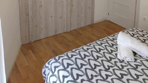 Een slaapkamer met een houten garderobe, een bed met beddengoed met een patroon, een witte deur en een plafondlamp.