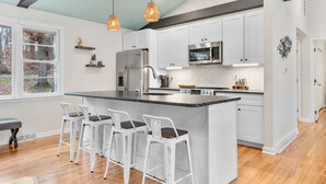 Una cocina moderna con armarios blancos, una isla grande con taburetes altos, electrodomésticos de acero inoxidable e iluminación colgante.