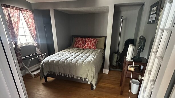 Un dormitorio con cama, suelo de madera, ventilador de techo, ventana con cortinas y una puerta.