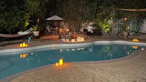 Una piscina con un deck circundante, mobiliario exterior y un fondo de bambú.