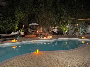 A swimming pool with a surrounding deck, outdoor seating, and a bamboo backdrop. - Oasis in Tarpon Springs (Tarpon Springs)