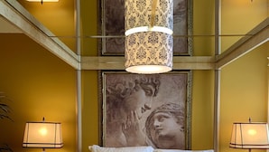 Una camera d'albergo con un letto grande, due lampade ai lati del letto, un elemento decorativo a parete e un lampadario.