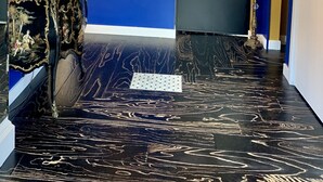 Un corridoio con pareti blu, pavimento in marmo nero, un tavolino decorativo con una lampada, un quadro e un televisore.