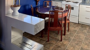 Una cucina con mobili bianchi, un fornello e un forno a microonde. C'è un tavolo da pranzo con sedie e una finestra con decorazioni.
