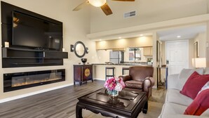 A modern living room with a fireplace, a flat-screen TV, and a ceiling fan. - Desert Paradise Retreat Awaits on Golf Course with Sunset & Mountain Views (Palm Desert)