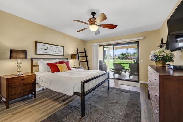 Une chambre à coucher comprenant un lit, une table de chevet, une commode, un ventilateur de plafond et une vue sur l’extérieur.