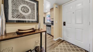 A hallway with a decorative wall piece, a wooden console table with a tray, and a white door. - Desert Paradise Retreat Awaits on Golf Course with Sunset & Mountain Views (Palm Desert)