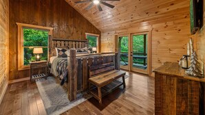 A wooden cabin interior with a bed, bench, and a ceiling fan. - Knotty Dreams - Luxury Awaits, Hot Tub, Party Porch (Mineral Bluff)