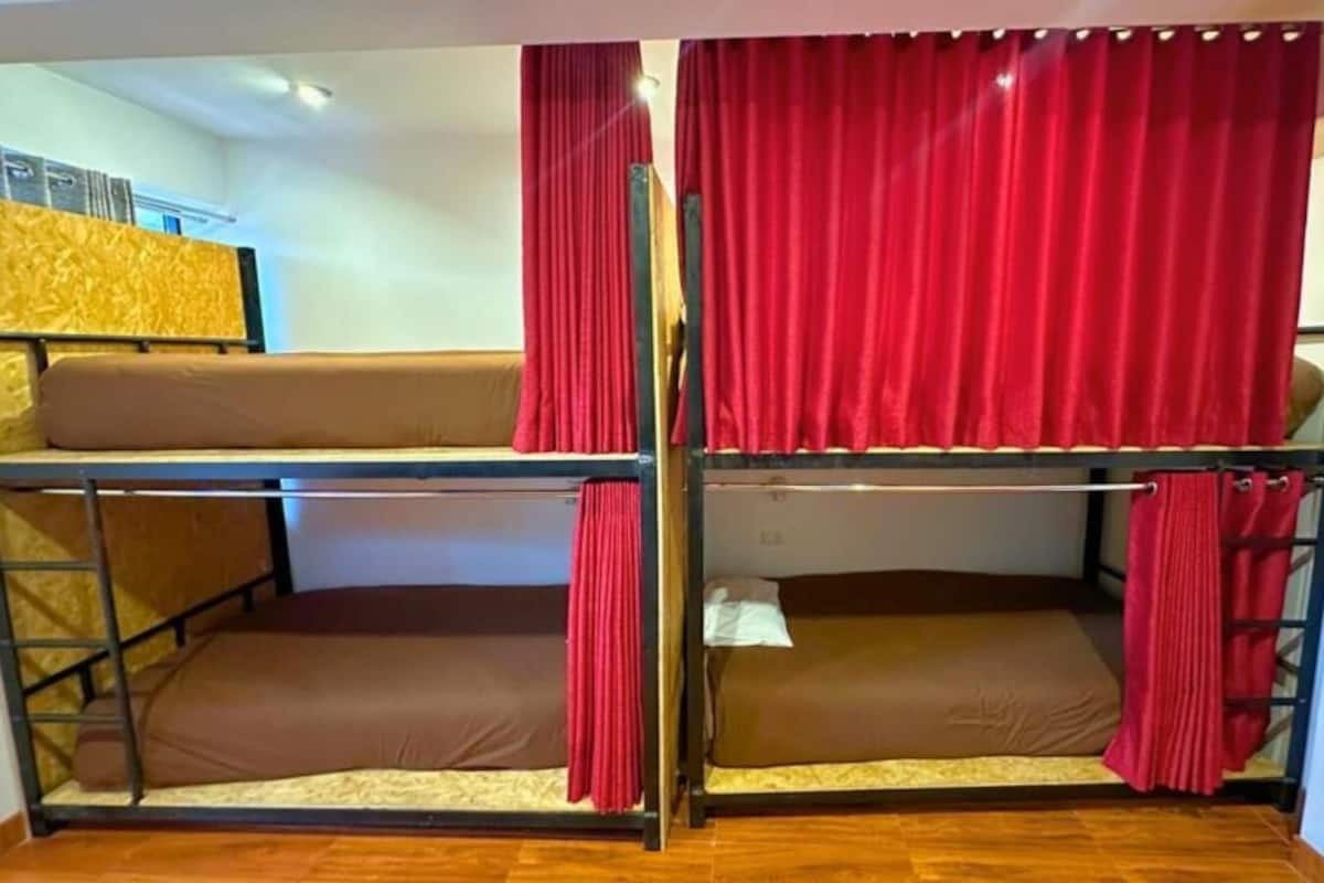 Habitación con literas, cortinas rojas, suelo de madera y una mesita.