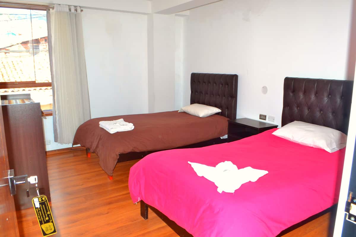 Habitación de hotel con dos camas, suelo de madera y vista a un edificio.
