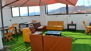 Une pièce dotée d’un sol recouvert d’un gazon synthétique vert, de canapés en cuir jaune et marron, d’une petite table et d’une grande fenêtre offrant une vue sur un paysage urbain et des montagnes.