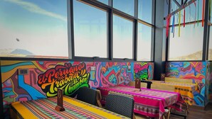 Un restaurant aux murs ornés de peintures murales colorées, aux tables recouvertes de nappes vives et offrant une vue sur les montagnes grâce à de grandes fenêtres.