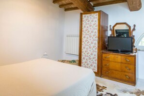A bedroom with a bed, wooden dresser, television, and a radiator.
