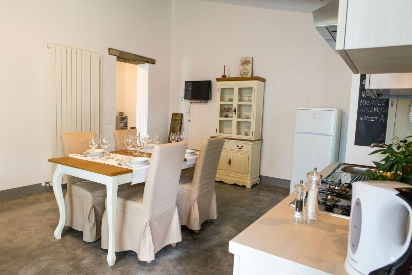 A dining area with a table set for four, a cabinet with glass doors, a television mounted on the wall, and a refrigerator.