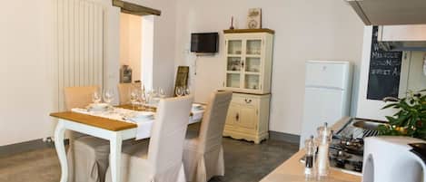 A dining area with a table set for four, a cabinet with glass doors, a television mounted on the wall, and a refrigerator.