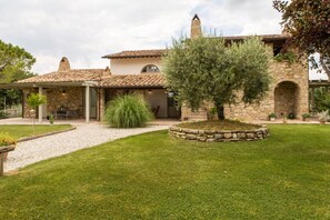 A stone house with a tiled roof, a covered patio, and a well-maintained lawn.