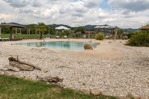 A pool area with a pebble ground, lounge chairs, and a pergola structure.