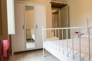 A bedroom with a white bed, a wardrobe, a mirror, and a small bedside table.
