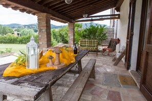 A covered outdoor seating area with a table, benches, and a view of the countryside.