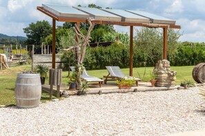 A gazebo with a transparent roof, two lounge chairs, and a stone pillar.