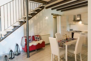 A modern interior with a staircase, a red sofa, a dining table with chairs, and a kitchen area.
