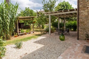 A covered patio area with a pergola, outdoor seating, and a gravel path.