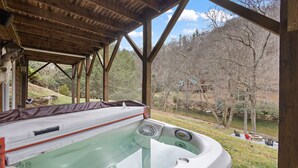 A hot tub under a wooden pergola with a view of a river and trees. - Riverfront Cabin with Hot Tub and Game Room (Boone)
