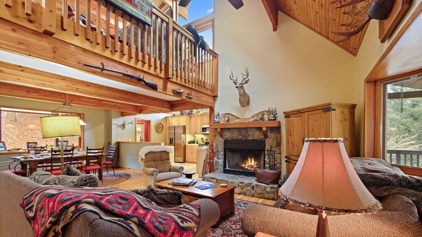 A cozy lodge interior with a fireplace, wooden furniture, and a balcony with a deer head decoration. - Riverfront Cabin with Hot Tub and Game Room (Boone)