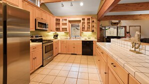 A kitchen with wooden cabinets, stainless steel appliances, and a tiled floor. - Riverfront Cabin with Hot Tub and Game Room (Boone)
