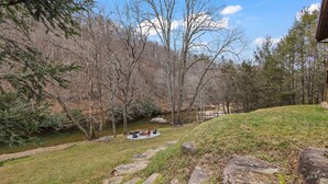 A riverside outdoor seating area with stone steps leading down to the water, surrounded by trees. - Riverfront Cabin with Hot Tub and Game Room (Boone)