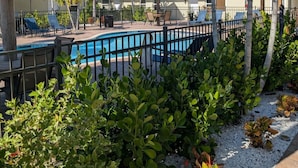 Un área de piscina con sillas de descanso, una sombrilla de paja y plantas tropicales.