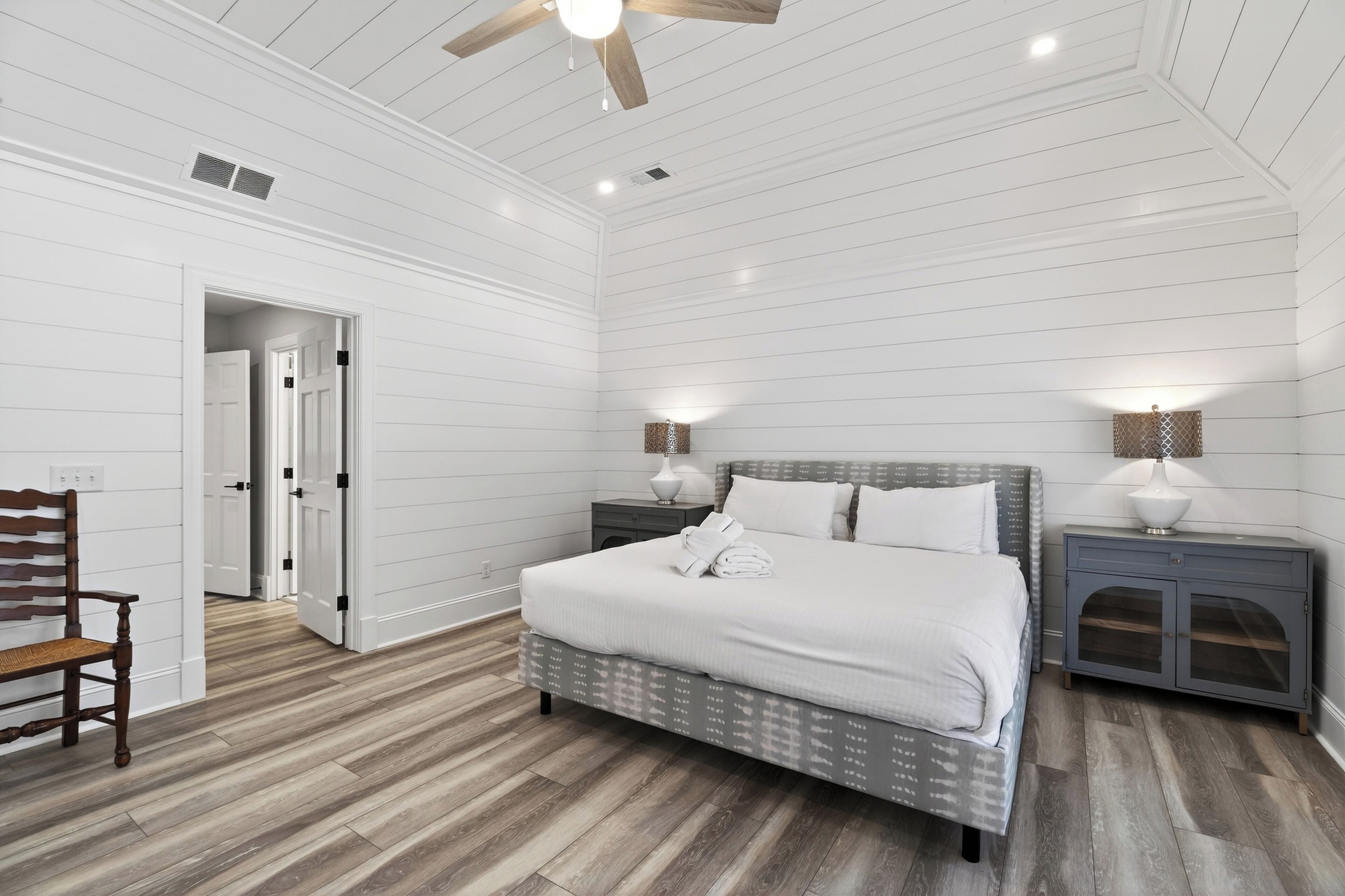 A bedroom with a bed, nightstands, a chair, and a door leading to another room.