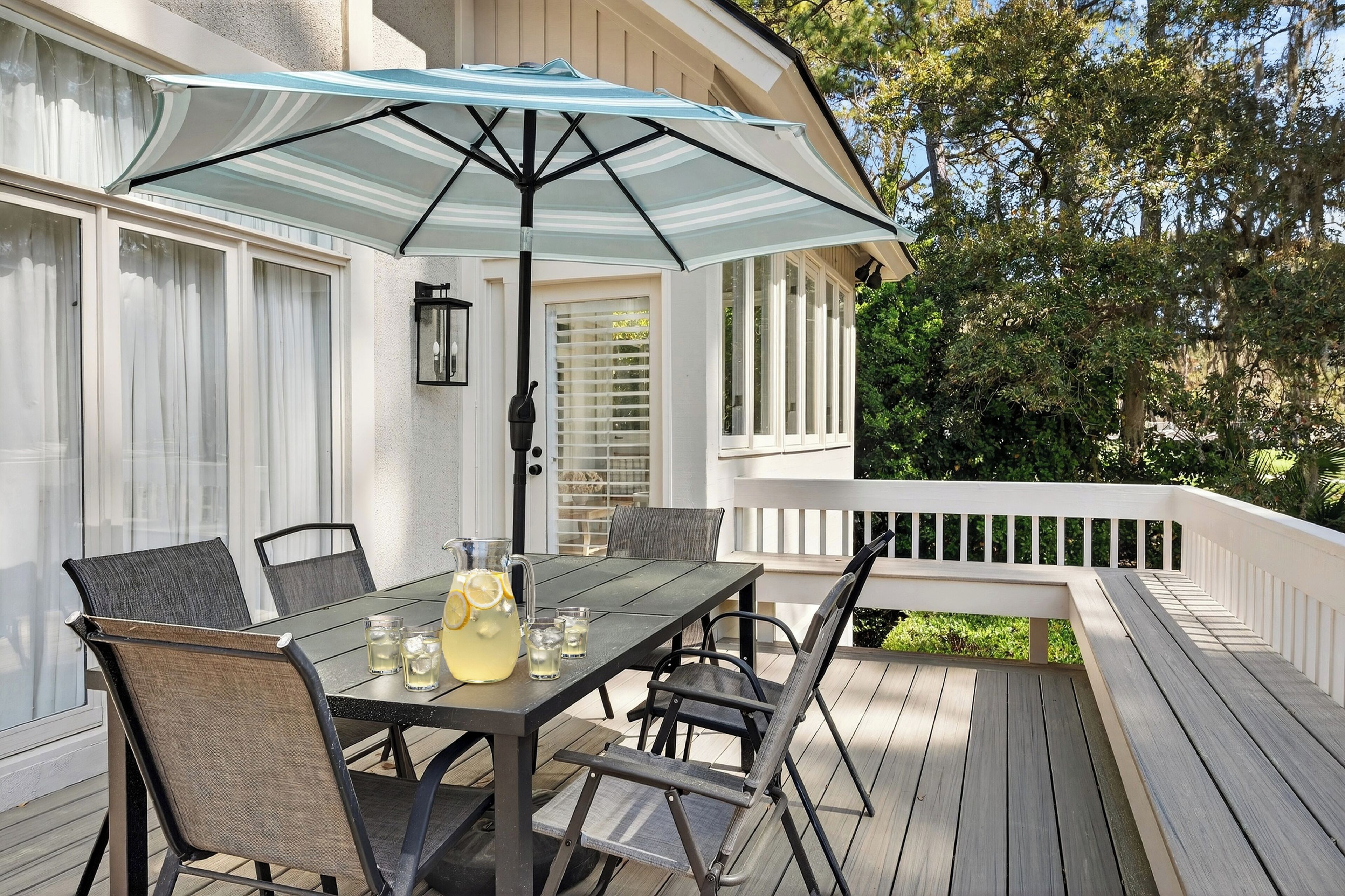 A deck with a table and chairs, an umbrella, and a white railing.