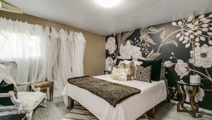 A bedroom with a bed, a chair, a table, and a wall with floral wallpaper. - Designer Condo in Hip Zen Yard! Midtown Phoenix! (Phoenix)