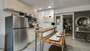 A modern kitchen with stainless steel appliances, a wooden dining table set with plates and cups, and a mirror on the wall. - Designer Condo in Hip Zen Yard! Midtown Phoenix! (Phoenix)