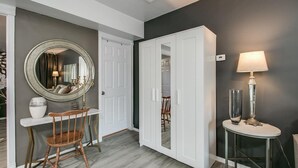 A hallway with a round mirror, a white door, a dining area with a chair, and a table with a lamp. - Designer Condo in Hip Zen Yard! Midtown Phoenix! (Phoenix)