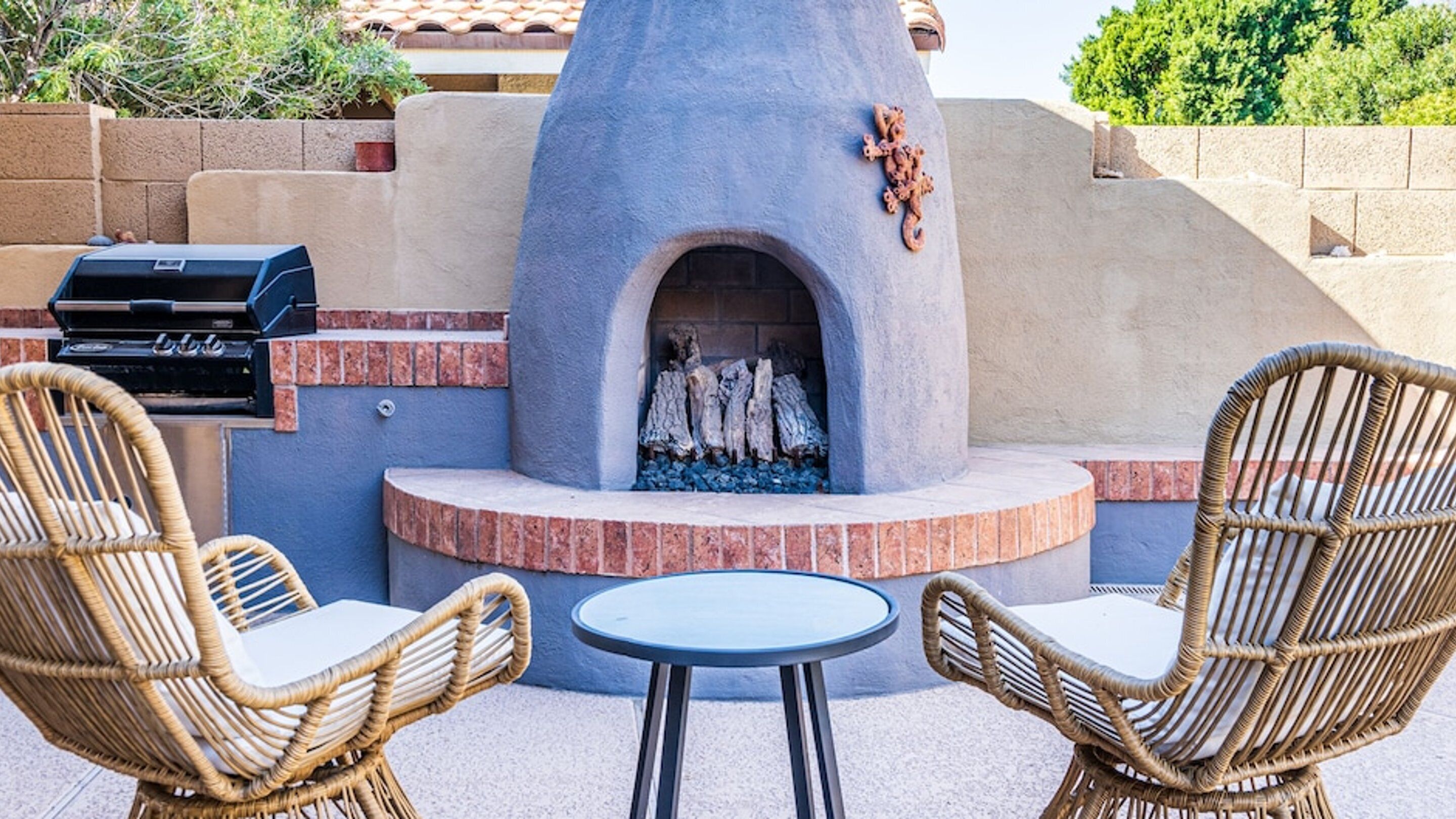 Eine Terrasse im Freien mit Kamin aus Stein, Korbstühlen und Grill.