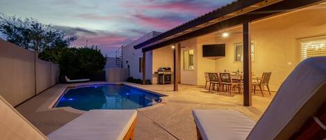 Ein Garten mit Swimmingpool, Liegestühlen, Grillplatz und Essbereich.