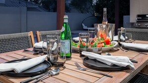 Ein Tisch, gedeckt für eine Mahlzeit, mit einer Flasche Crino Wein, Gläsern und einer Schüssel mit Obstsalat.