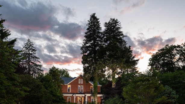 A large brick house with a well-maintained lawn and tall trees in the foreground. - South Court Inn (Luray)
