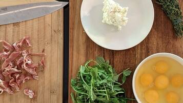 Una tabla de madera con un cuchillo, carne picada, vegetales frescos, un cuenco de huevos y un plato con una sustancia blanca.