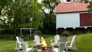 A fire pit with four Adirondack chairs around it, set in a grassy area with a barn in the background. - South Court Inn (Luray)