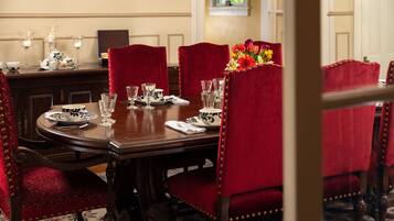 A formal dining room with a wooden table set for four, red upholstered chairs, and a vase of flowers.