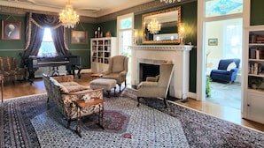 A classic living room with a grand piano, a fireplace, and elegant chandeliers. - South Court Inn (Luray)
