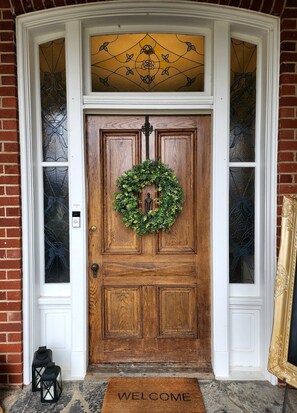 A wooden front door with a wreath, a welcome mat, and a bell.