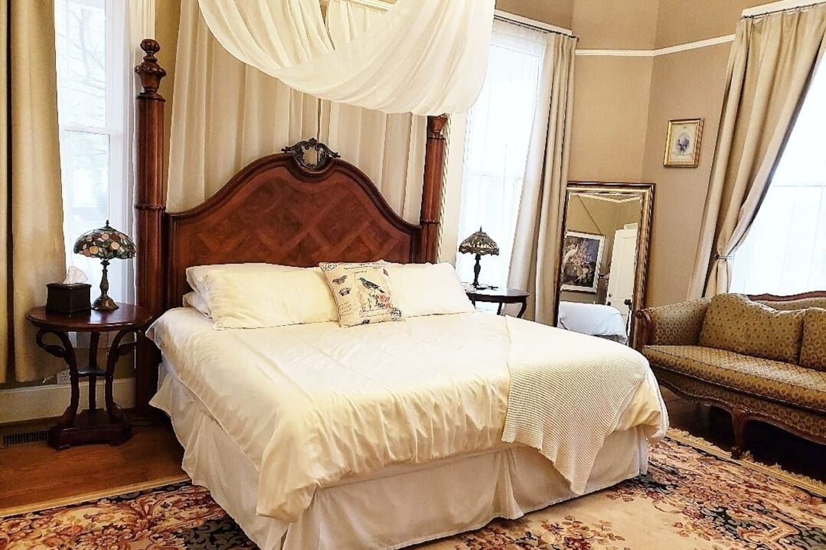 Un dormitorio amplio con una cama grande, dosel, sofá y espejo.
