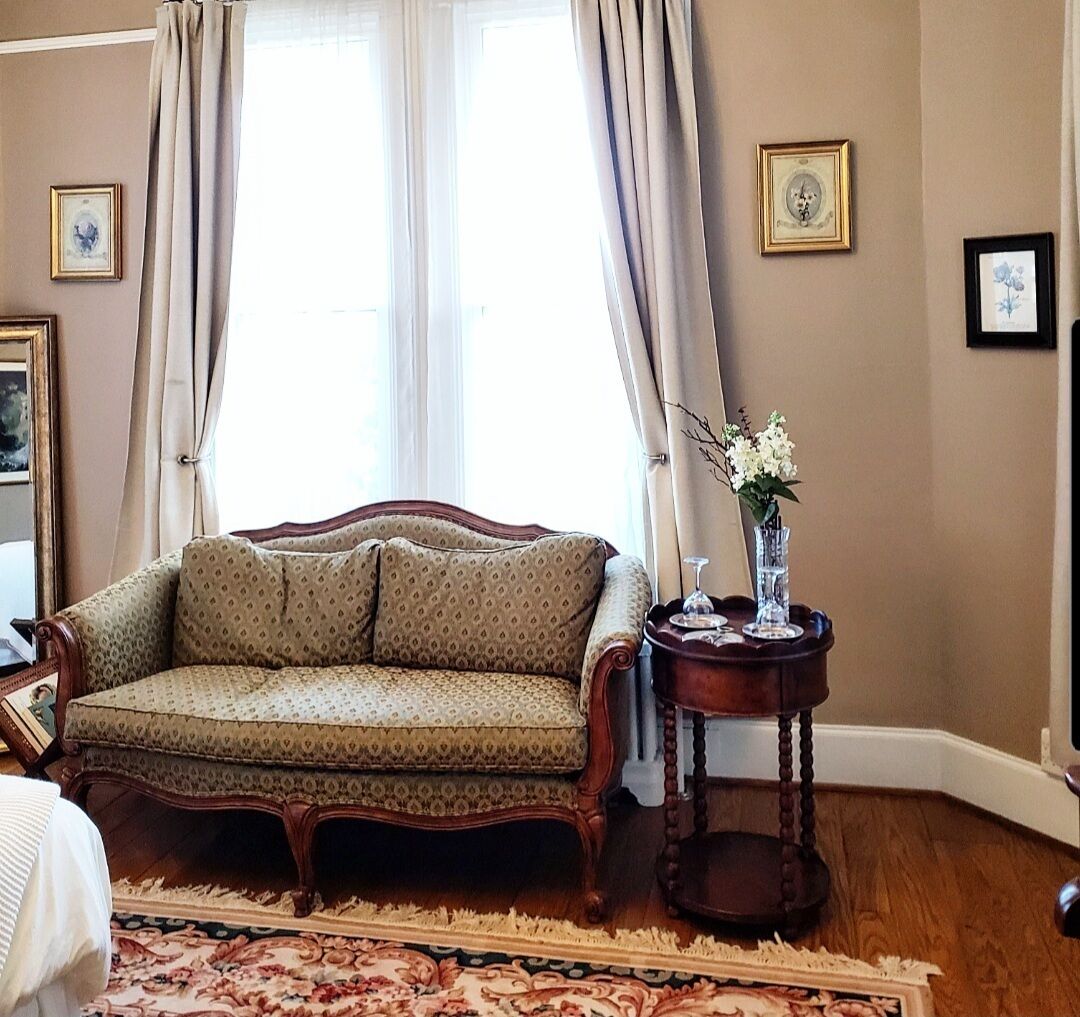 A room with a sofa, a small side table, a vase with flowers, and framed pictures on the wall.