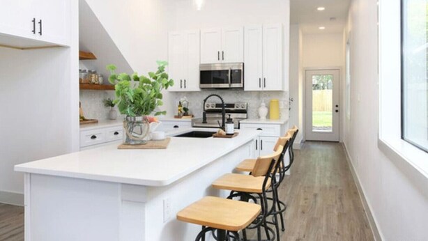 A modern kitchen with white cabinetry, a central island with bar stools, and a large window providing natural light.