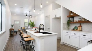 A modern kitchen with white cabinetry, a central island with stools, pendant lighting, and a view of the dining area.