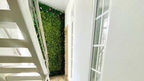 A narrow hallway with a staircase on the left, a green wall with flowers, and a window on the right.